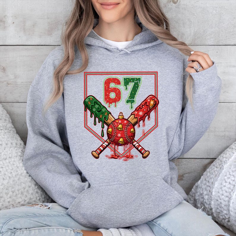 May include: A gray hoodie featuring a baseball-themed graphic. The graphic includes crossed baseball bats, a baseball with red accents, and the number "67" in red and green. The design has a festive, holiday theme.