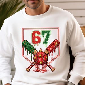 A holiday-themed design featuring the number 67 in a dripping, frosted style over crossed baseball bats. A baseball, decorated as a festive ornament with jingle bells and snowflakes, sits at the center. The bats are also coated in melting holiday icing.