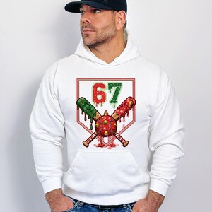 May include: White hoodie with a graphic featuring crossed baseball bats, a baseball, and the number 67 in red and green. The bats are decorated with red and green accents. The design is set against a white background.