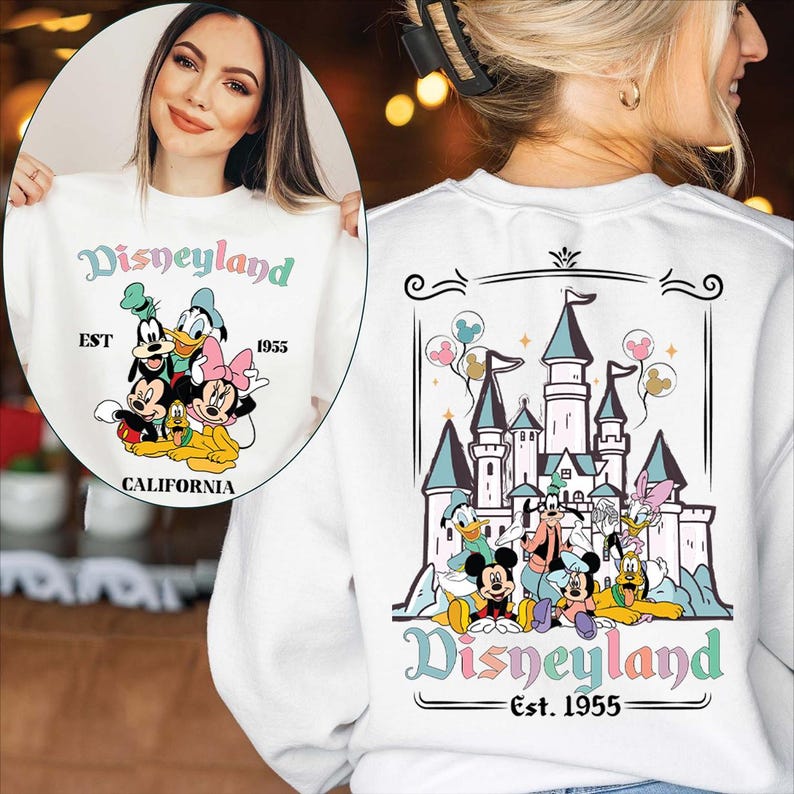 Puede incluir: Sudadera blanca con dise&ntilde;o de Disneyland. La parte delantera muestra la palabra "Disneyland" en colores pastel, con Mickey Mouse, el Pato Donald y otros personajes. La parte trasera muestra un castillo y personajes, con "Disneyland Est. 1955."