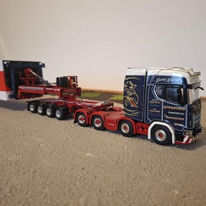 Op de afbeelding: Een gedetailleerd model van een vrachtwagen met oplegger. De cabine is marineblauw en wit met rode accenten, met de tekst "McFadyens Transport Ltd." De oplegger is rood en wit.