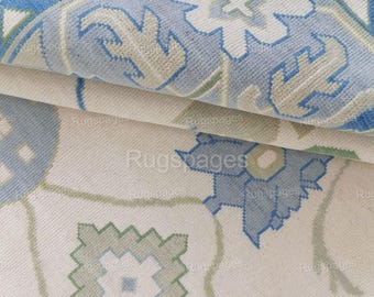 May include: A close-up of a white rug with a blue and green geometric pattern. The rug has a soft, textured surface.