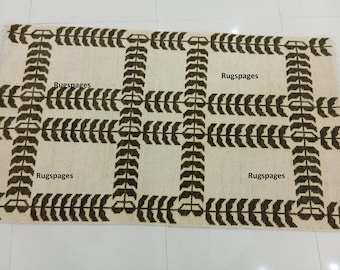 May include: A beige and brown area rug with a geometric pattern of repeating leaf shapes. The rug has the text "Rugspaces" printed four times on the rug.