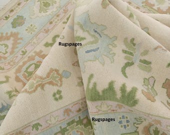 Puede incluir: Una alfombra de color crema con un patrón floral en tonos verdes, azules y rosas. La alfombra está doblada por la mitad, mostrando los intrincados detalles del diseño.