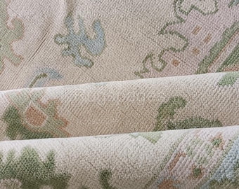 Puede incluir: Primer plano de una alfombra de color crema con un patrón geométrico en tonos de verde, azul y melocotón. La alfombra está doblada por la mitad, revelando la parte inferior.