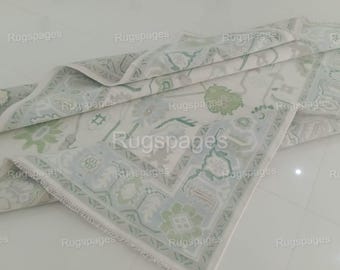 Puede incluir: Una alfombra blanca y verde con estampado y borde de flecos. La alfombra está doblada por la mitad y el estampado es visible en ambos lados.