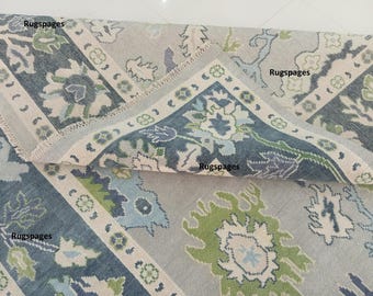 Puede incluir: Una alfombra de color azul y verde con fondo crema. La alfombra tiene un diseño floral con un patrón repetitivo. La alfombra está doblada por la mitad, mostrando el reverso de la alfombra.