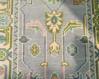 Puede incluir: Una alfombra azul con un patrón floral en tonos de verde, rosa y blanco. La alfombra tiene un diseño geométrico con un motivo central de flor.