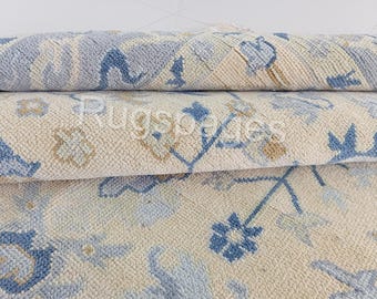 Könnte beinhalten: Nahaufnahme eines aufgerollten Teppichs mit floralem Muster. Der Teppich hat einen cremefarbenen Hintergrund mit blauen und beigen floralen Designs. Die Textur des Teppichs ist sichtbar, und das Design wiederholt sich in den gerollten Abschnitten.