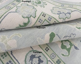 Puede incluir: Primer plano de una alfombra de color azul claro y blanco con detalles verdes. La alfombra está doblada en tres partes, mostrando el patrón en cada capa.