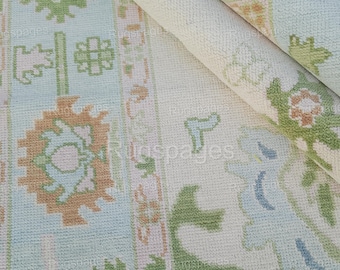 Puede incluir: Primer plano de una alfombra de color crema con un patrón floral de color azul claro, verde y melocotón. La alfombra tiene un brillo sutil y una textura suave.