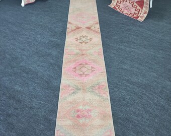 Puede incluir: Una alfombra de pasillo larga y estrecha con un esquema de color rosa y beige. La alfombra tiene un patrón geométrico tradicional con detalles intrincados.