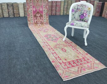 Puede incluir: Una alfombra larga y estrecha de color rosa y beige con un diseño floral. La alfombra está colocada sobre un suelo gris oscuro con una silla blanca con un asiento de estampado floral en el fondo.