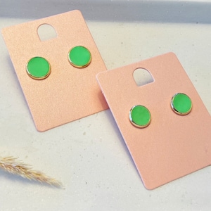 Könnte beinhalten: Zwei Paare grüne und goldene Ohrstecker auf rosa Karton.