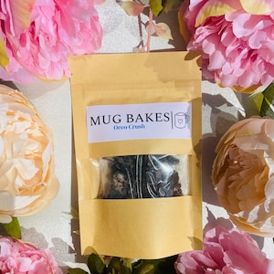 May include: A brown paper bag with a white label that says "MUG BAKES" and "Oreo Crush". The bag contains a clear plastic bag with a dark brown mixture inside.