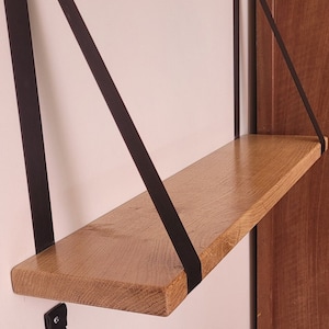 Peut inclure: Une étagère en bois avec des sangles en cuir noir suspendues au mur. L'étagère est en bois naturel et a un aspect rustique.