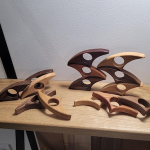 May include: A set of wooden stacking toys in various shades of brown. The pieces are shaped like crescent moons with a hole in the centre. The toys are arranged in a stack and scattered on a wooden surface.