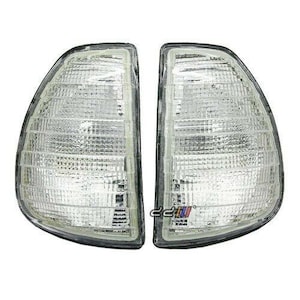 May include: A pair of white clear plastic car headlights with a black trim. The headlights are rectangular in shape and have a grid pattern.