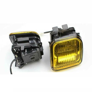 May include: A pair of yellow fog lights with black housings. The lights are rectangular and have a grid pattern on the lens.