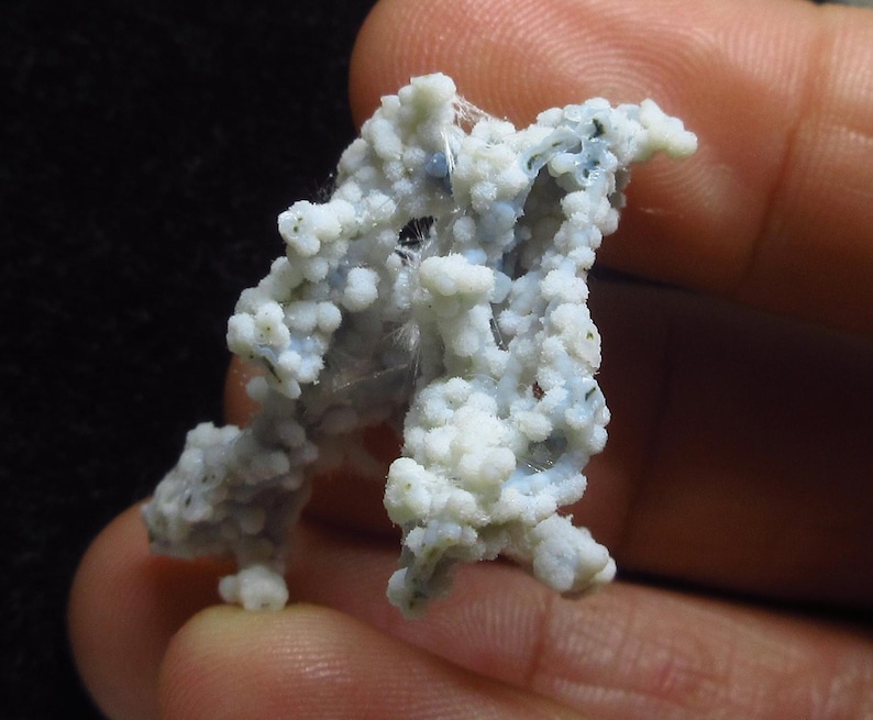 May include: A close-up of a mineral specimen featuring a cluster of small, round, white and light blue formations. The mineral has a textured, porous appearance, with some areas appearing translucent. The background is dark.