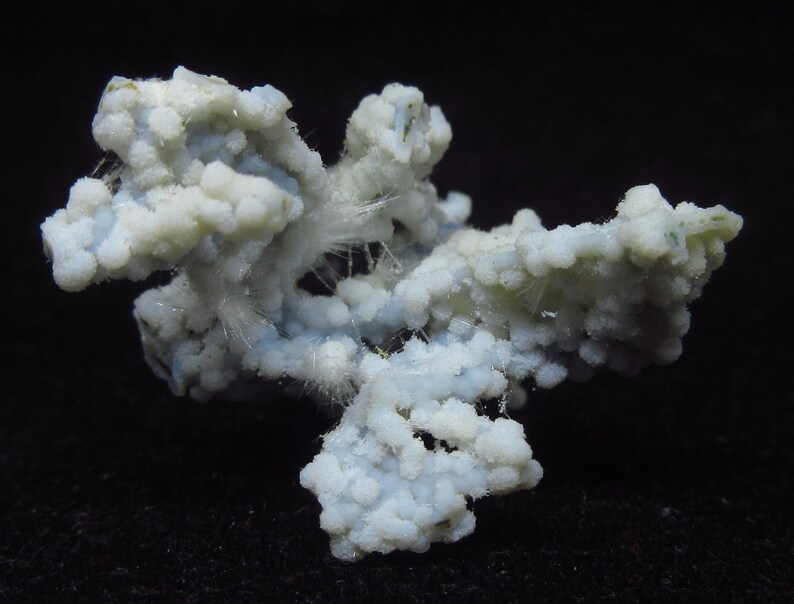 May include: A close-up of a mineral specimen with a complex, branching structure. The mineral has a pale blue and white color, with a textured, almost bubbly appearance. Fine, hair-like crystals are visible throughout the structure, set against a black background.