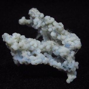 May include: A close-up of a light blue and white mineral specimen. The mineral has a bubbly, textured appearance with small, rounded formations clustered together. Fine, white, thread-like structures are visible throughout the specimen. The background is black.