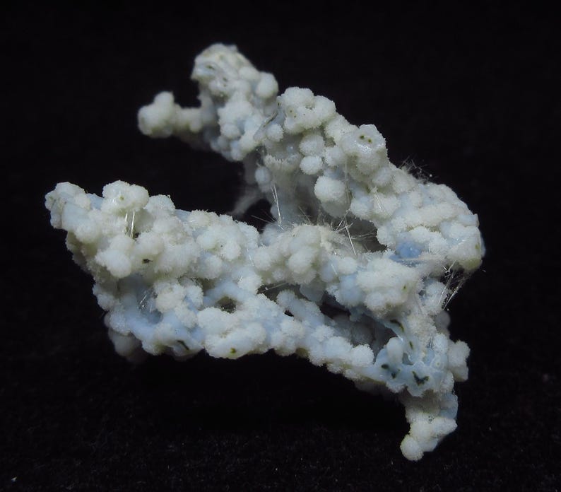 May include: A close-up of a light blue and white mineral specimen. The mineral has a bubbly, textured appearance with small, rounded formations clustered together. Fine, white, thread-like structures are visible throughout the specimen. The background is black.