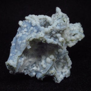 Puede incluir: Una geoda de &aacute;gata azul y blanca con una formaci&oacute;n cristalina en su interior. La geoda est&aacute; cubierta de peque&ntilde;os cristales blancos y tiene una superficie rugosa y texturizada.