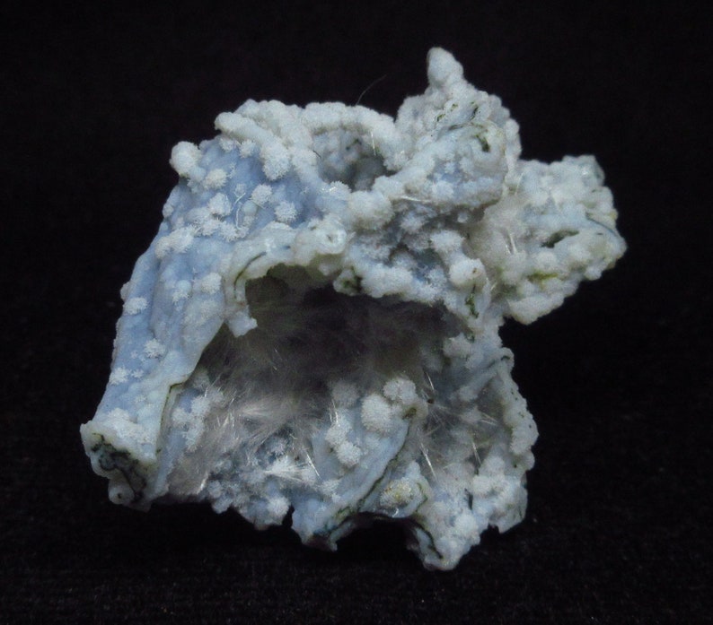 Puede incluir: Una geoda de &aacute;gata azul y blanca con una formaci&oacute;n cristalina en su interior. La geoda est&aacute; cubierta de peque&ntilde;os cristales blancos y tiene una superficie rugosa y texturizada.
