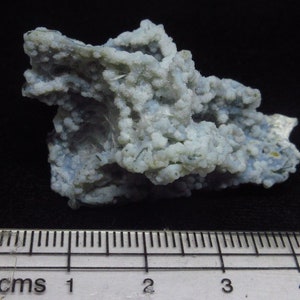 Puede incluir: Una geoda de &aacute;gata azul claro y blanco con una superficie rugosa y texturizada. La geoda mide aproximadamente 2,5 cm de ancho y est&aacute; sobre una regla.