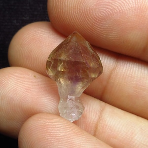 以下が含まれることがあります： 紫色と黄色の色合いの透明な水晶。結晶はファセットカットされており、先端が尖っています。高さは約2.5cmです。
