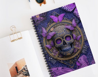 May include: A spiral-bound notebook featuring a detailed illustration of a skull with purple eyes and butterfly accents. The design is set against a dark blue background with floral patterns and additional purple butterflies. The notebook is open on a white surface.