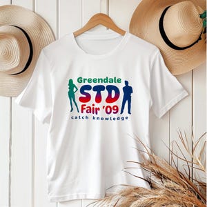 Greendale STD Fair Shirt | Community TV Show Inspired T-Shirt | Funny Catch Knowledge Tee | Pop Culture Fan Gift | Unisex Graphic Tee