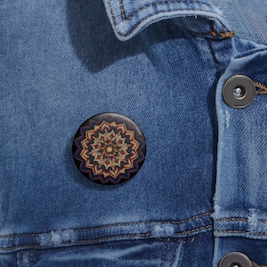 Op de afbeelding: Een ronde knoop met een kleurrijk mandala-ontwerp. De mandala is in tinten oranje, geel, blauw en groen. De knoop is zwart en heeft een glanzende afwerking.