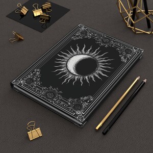 Let your thoughts drift into the mystical with this Gothic Sun & Moon Eclipse Journal. The ornate vintage border and celestial centerpiece make it the perfect notebook for witches, poets, and dark academia lovers alike.