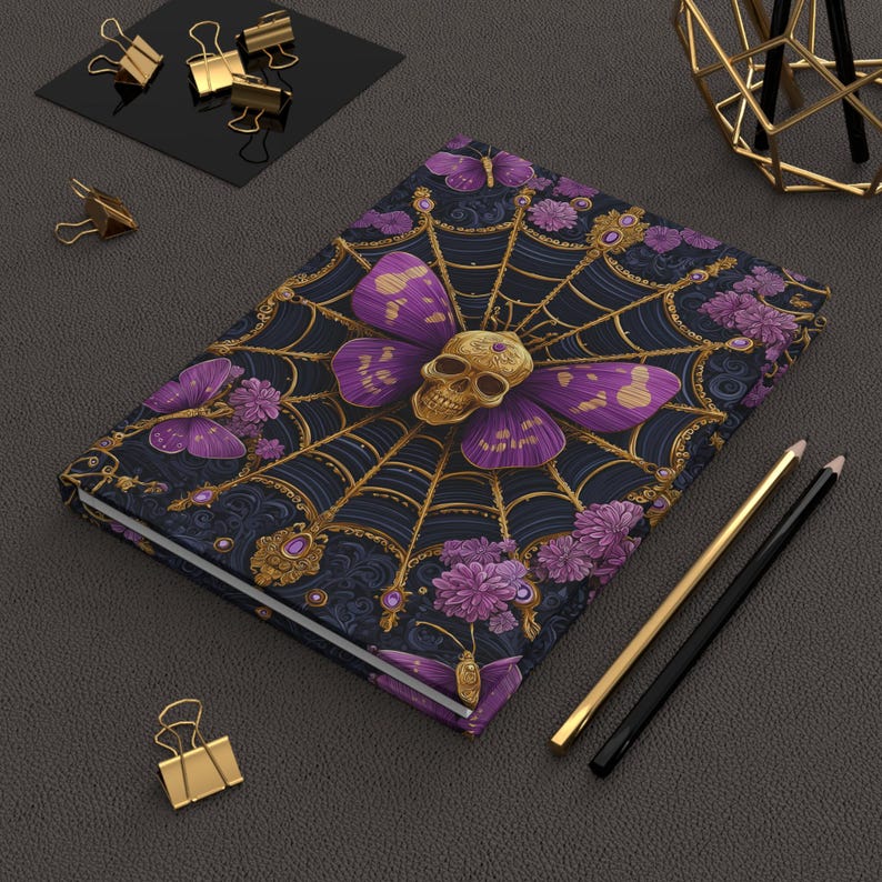 Hardcover journal featuring an ornate gothic design of a golden skull with purple butterfly wings at the center of a golden spiderweb. Surrounded by rich purple flowers, butterflies, and intricate details, all set against a dark, swirling background.