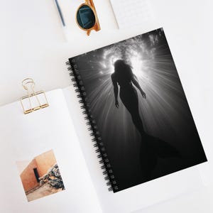 May include: Black and white photo of a mermaid silhouette swimming underwater with sunlight shining through the water.