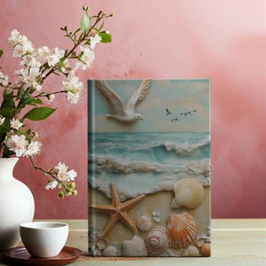 May include: A hardcover journal with a matte finish featuring a seashell and starfish design. The cover has a seagull flying over a blue ocean wave. The journal has 150 lined pages and measures 5.75 inches by 8 inches.