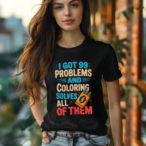 May include: Black t-shirt with the text "I GOT 99 PROBLEMS AND COLORING SOLVES ALL OF THEM." The design includes a colorful illustration of crayons. The shirt is a crew neck style.