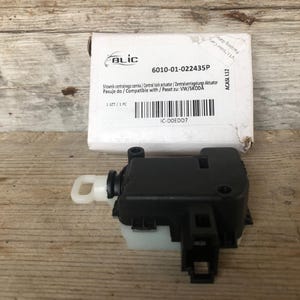 Puede incluir: Un actuador de cierre centralizado negro con una palanca blanca, junto a una caja blanca con el texto "BLIC" y "6010-01-022435P". La caja también incluye texto en varios idiomas y un código de barras. El actuador es para vehículos VW/SKODA.