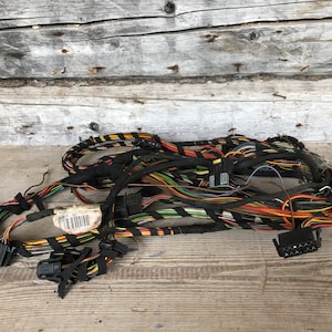 Puede incluir: Un haz de cables eléctricos, cables y conectores multicolores. Los cables son negros, rojos, amarillos, verdes, azules y otros colores. Los conectores son negros. Los cables están sobre una superficie de madera desgastada.