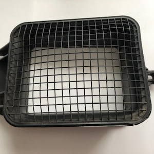 May include: A black rectangular air vent cover with a grid pattern. The cover has a square shape with rounded corners and a raised edge. The grid is made of thin, intersecting lines, creating a mesh-like appearance. The vent cover is made of plastic.