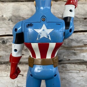 May include: A blue Captain America action figure, viewed from the back. The figure has a white star on the chest, red and white stripes on the torso, and red gloves. The figure is made in China.