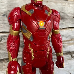 May include: A red and gold Iron Man action figure. The figure has a light-up chest piece and detailed armor design. The figure is approximately 12 inches tall.