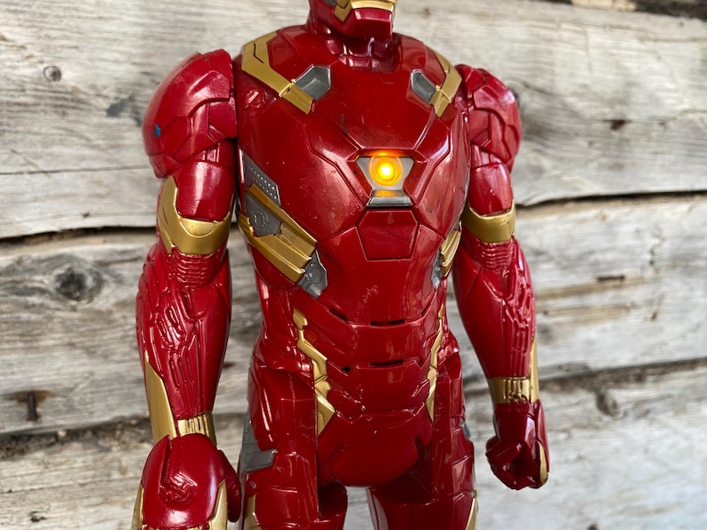May include: A red and gold Iron Man action figure. The figure has a light-up chest piece and detailed armor design. The figure is approximately 12 inches tall.