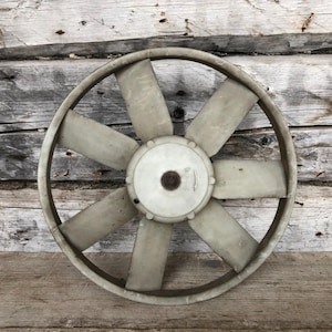 May include: A large, circular fan with eight blades and a central hub. The fan is a light gray color and appears to be made of plastic. It is set against a weathered, wooden background.