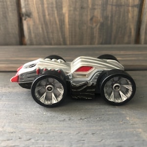 May include: A silver and red toy car with black wheels. The toy car has a detailed design with a red front bumper and a red accent on the top. The wheels have a silver hubcap design.