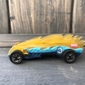 May include: A toy car with a yellow and blue design, featuring the number 4 and the Marvel Heroes logo. The car has black wheels and a flame-like design on top.