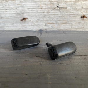 May include: Two black plastic windshield washer nozzles. Each nozzle has two small spray holes and a rounded, oblong shape. The nozzles are designed to spray fluid onto a vehicle's windshield.