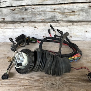 Puede incluir: Un surtido de mazos de cables automotrices negros, conectores y fuelles de goma. Los cables son multicolores y los componentes están dispuestos sobre una superficie de madera envejecida.